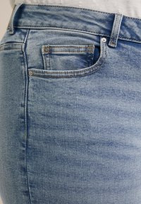 Světle modré džíny z denimového materiálu s vybledlým povrchem, obsahující malou přední kapsu, viditelné švy a klasický design pěti kapes.