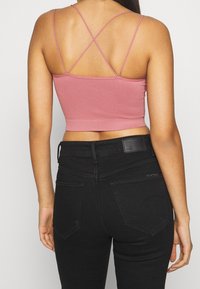 Růžový crop top s jemnými prokrývajícími ramínky, spárovaný s černými džíny s vysokým pasem, které mají zadní kapsy a koženou nášivku.