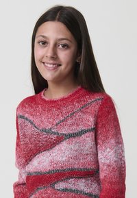 Maglione rosso a maglia con un motivo a gradient con sottili strisce nere, scollatura rotonda e finitura testurizzata. Indossato da un bambino.