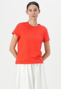 Tricou roșu din bumbac, cu mâneci scurte și decolteu rotund, asociat cu o fustă albă fluidă. Textură netedă, design simplu.