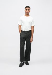 Balta kokvilnas T-krekls ar brīvu piegriezumu; tumši pelēkas teksturētas bikses ar taisnām kājām, jostu un melnas slip-on kurpes, stāv uz baltas fona.