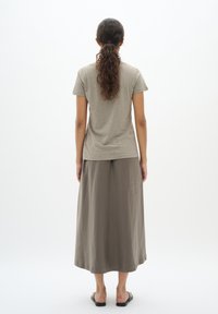 Olijfgroen T-shirt met korte mouwen, gecombineerd met een lange, vloeiende taupe rok. De stoffen lijken zacht, met subtiele textuurvariaties en een ontspannen pasvorm.