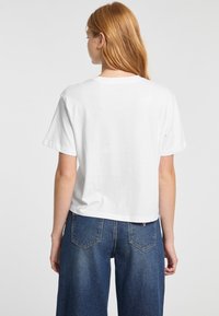 Camiseta blanca de algodón con mangas cortas y un diseño recortado, combinada con unos vaqueros de mezclilla azul de cintura alta que cuentan con bolsillos traseros.