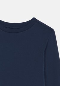 Laivastonsininen pitkähihainen paita, jossa on pyöreä kaula-aukko. Pehmeä puuvillakangas, sileä tekstuuri ja minimaalinen ommel yksityiskohtana olkapään lähellä.