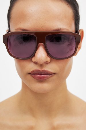 Gafas de sol marrones de gran tamaño con un marco grueso y lentes tintados en púrpura, con un acabado brillante y forma rectangular.