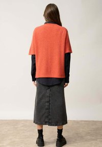 Suéter naranja de punto oversized con mangas cortas, combinado con una falda larga de denim negra y zapatos negros de suela gruesa. Diseño sencillo, textura suave.