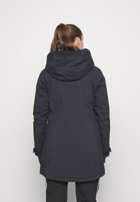 Parka noir, isolée, avec une grande capuche, des poignets ajustables et une coupe droite. Ses caractéristiques comprennent une taille avec cordon de serrage et des poches latérales.