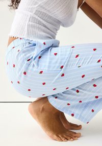 Ανοιχτό μπλε ριγέ παντελόνια πυτζάμας με μικρά κόκκινα σχέδια φράουλας. Διαθέτουν ελαστική μέση και άνετη, φαρδιά γραμμή στο πόδι.