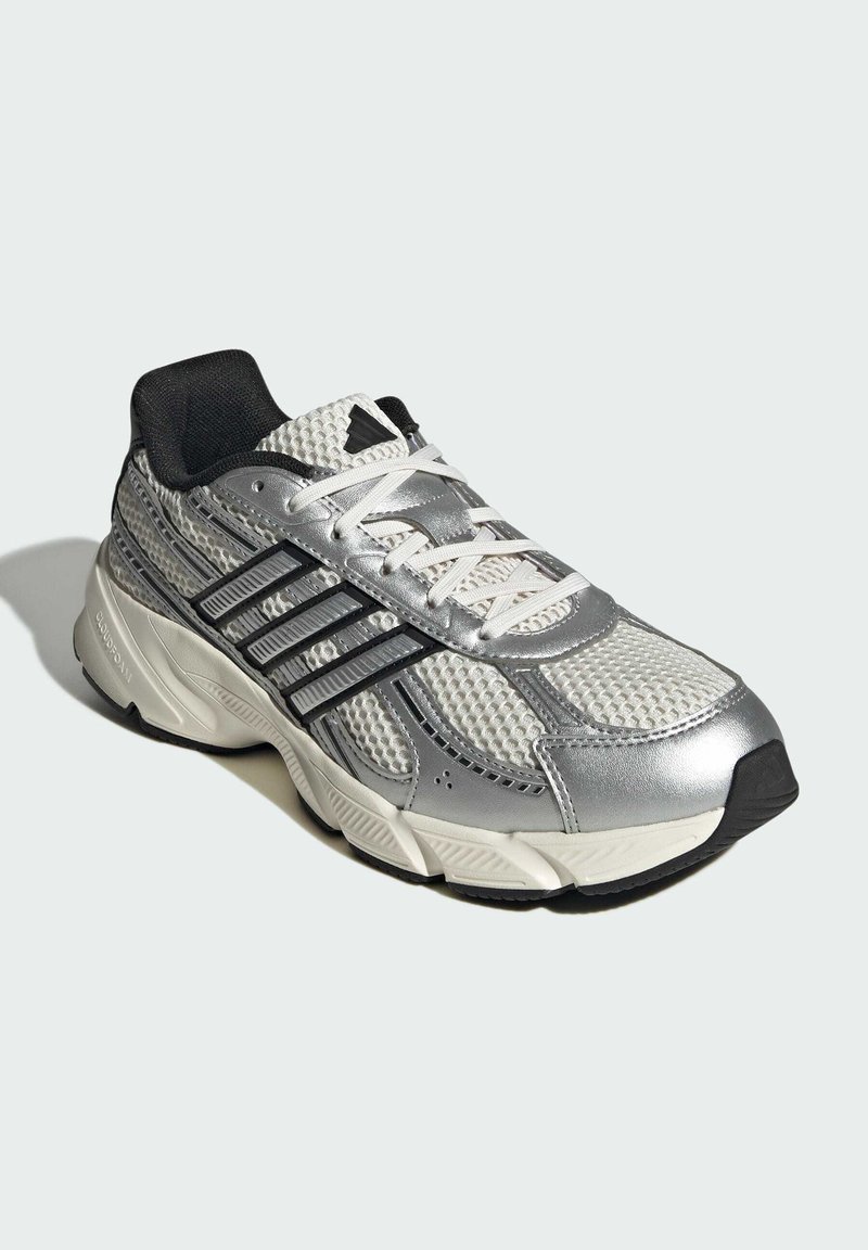 Grijs en zilveren sportieve schoen met een bovenwerk van mesh, zwarte accenten en een dikke rubberen zool. Geknoopt met witte veters en heeft opvallende strepen.