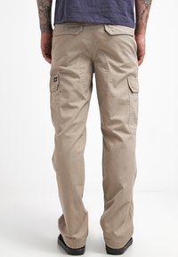 Beige cargo pants made from textured fabric, featuring side pockets and a straight cut, combined with black footwear.