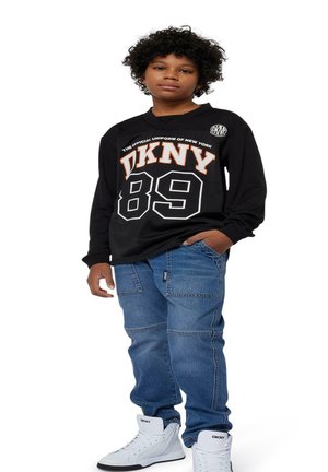 Maglietta nera a maniche lunghe con stampa bianca e arancione "DKNY 89"; pantaloni cargo in denim blu; sneakers alte bianche con logo DKNY.