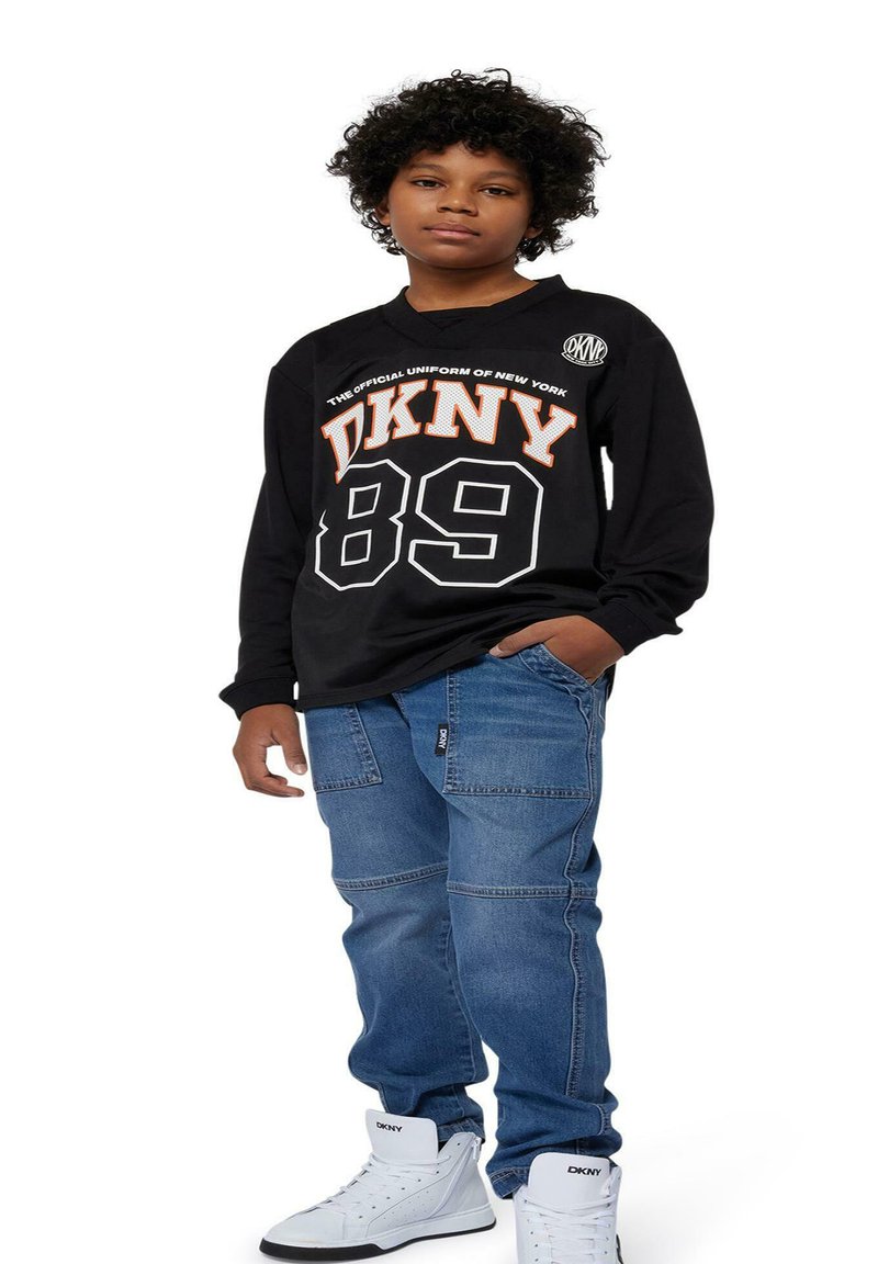 T-shirt noir à manches longues avec impression blanche et orange "DKNY 89" ; pantalons cargo en denim bleu ; baskets montantes blanches avec logo DKNY.
