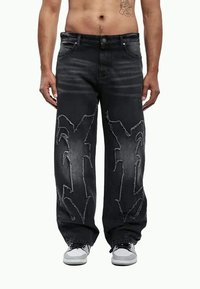 Calças de ganga pretas com corte descontraído, apresentando detalhes desgastados e padrões de costura brancos. Bolsos frontais e fecho com botão.