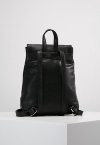 Sac à dos en cuir noir à texture lisse, avec double poignées supérieures, bretelles ajustables et design minimaliste.
