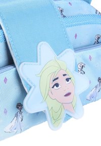 Niebieski plecak z nylonu z zawieszką w kształcie gwiazdki z rysunkową twarzą. Tkanina ma małe nadruki postaci i diamentów w kolorze fioletowym.