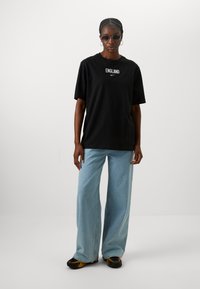 Black cotton t-shirt with "ENGLAND" text and Nike logo, paired with light blue wide-leg jeans and black shoes with yellow accents.