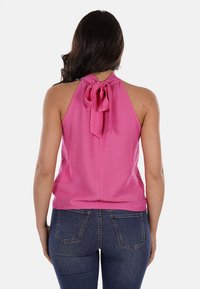 Top rosa a halter con un nodo al collo, realizzato in un tessuto leggero. Il retro presenta una superficie liscia e una vestibilità leggermente ampia. Abbinato a jeans.