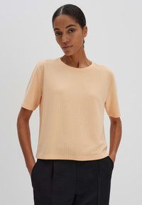 T-shirt rosa a maniche corte con motivo testurizzato, scollo rotondo, vestibilità rilassata e spacchi laterali. Abbinato a pantaloni neri eleganti.