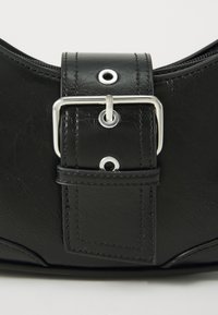 Svart konstläderväska med en framträdande silverbuckle, med en slät yta, sömnadsdetaljer och en zippered öppning.