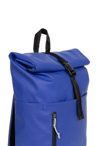 Blå rulltop ryggsäck med en strukturerad yta, svarta remmar, en sidofack med dragkedja och en säker spänneförslutning.