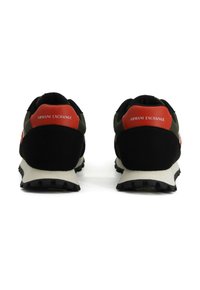 Une paire de sneakers noires et vert olive avec des languettes arrière rouges portant l'inscription "Armani Exchange" montrées de l'arrière sur un fond blanc.