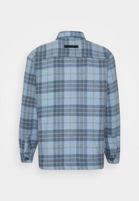 Camicia a maniche lunghe a quadri blu e grigia vista da dietro, con polsini bottonati e una piccola etichetta nera sotto il colletto.