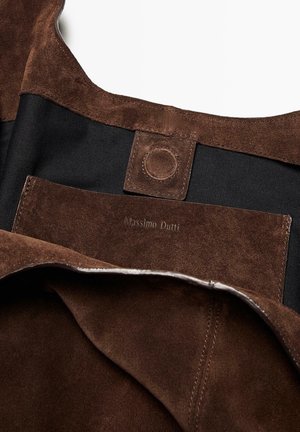 Brun ruskinds taske indvendigt med sort stofforing. Indeholder et debosseret logo og en tryklåsdetalje. Struktureret finish er tydelig.