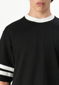 Sort oversized t-shirt med hvid ribkant ved kraven og hvide striber på ærmerne. Fremstillet af bomuld med en glat tekstur.