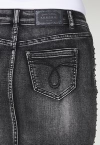 Gros plan de la poche arrière d'un jean en denim noir délavé avec une couture décorative et une étiquette de marque Koroshi sur la ceinture.