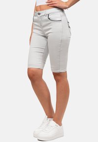 Bermuda shorts in denim grigio chiaro con un design aderente, tasche standard e accenti di cuciture nere, abbinati a sneakers bianche.