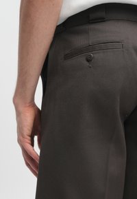 Σκούρο καφέ κομμένα παντελόνια από υφασμάτινο ύφασμα, με πίσω τσέπη που κλείνει με κουμπί και λείο ζωνάκι στη μέση.