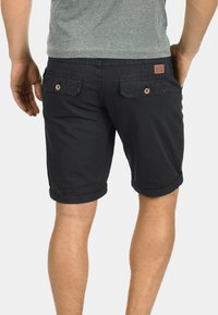 Pantalones cortos de algodón azul marino con puños enrollados, que cuentan con dos bolsillos traseros con cierres de botón y una pequeña etiqueta de la marca en la cintura.