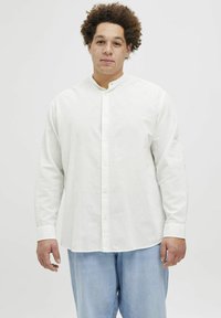 Weißes Langarmhemd mit Stehkragen, mit Knopfleiste, aus leichtem Stoff. Trägt es mit hellblauen Jeans.