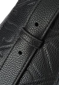 Czarna skórzana torebka z teksturowaną powierzchnią i paskiem zapinanym na klamrę z otworami do regulacji długości. Widoczny charakterystyczny wzór ziaren skóry.
