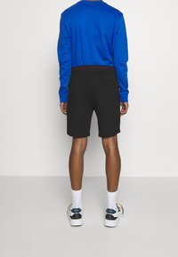 Chemise bleue à manches longues, short noir et baskets blanches. La chemise a un col rond, tandis que le short arrive aux genoux et possède une poche arrière.