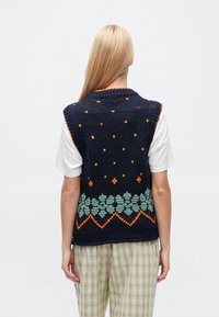 Granatowa, bezrękawnikowa, dzianinowa kamizelka z wzorzystym obszyciem w zielone, pomarańczowe i żółte akcenty. Teksturowana tkanina z okrągłym dekoltem i luźnym krojem.