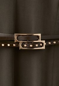 Cintura marrone scuro con fibbia rettangolare dorata e borchie in metallo, allacciata su tessuto scuro abbinato.