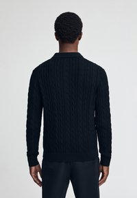 Svart stickad tröja med ett kabelmönster, ribbade muddar och nederkant samt krage. Baksidan visar den texturerade designen.