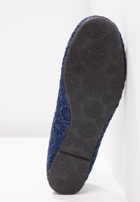 Semelle d'une chaussure plate bleu marine en crochet avec une semelle extérieure en caoutchouc à motif floral, taille 37, présentée sur un fond blanc en angle.