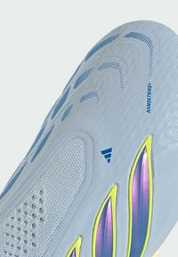 Gros plan sur la tige d'une chaussure de sport gris clair avec un mesh bleu, le texte bleu "NANOSTRIKE+" et des accents de design irisés en violet et jaune.