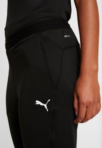 Zwarte sportbroek met een aansluitend ontwerp, gemaakt van rekbare stof. Kenmerkt een wit Puma-logo en een gestructureerde tailleband met het label "DRYCELL."