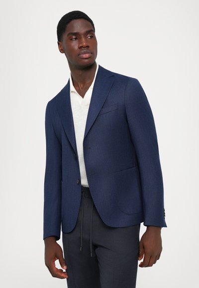 Blazer bleumarin cu un finisaj texturat, design cu un singur rând de nasturi, două buzunare frontale și o cămașă albă cu guler dedesubt. Stil slim-fit.