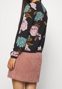 Top nero a maniche lunghe con motivo floreale, caratterizzato da fiori rosa, blu e gialli; abbinato a una gonna in corduroy rosa strutturato.