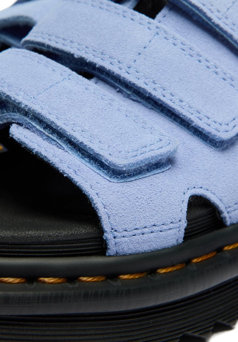 Close-up of light blue suede sandal straps with hook-and-loop fasteners and black sole with visible orange stitching.