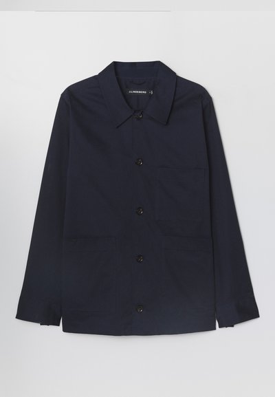 Marinblå bomullsjacka med spridd krage, framknäppning med knappar och två framsydda fickor. Har långa ärmar med knäppning vid cuffs.