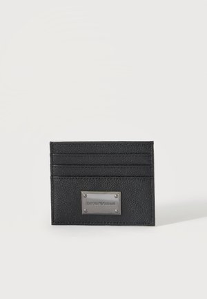 Portacarte in pelle nera con quattro scomparti per carte e una targhetta in metallo incisione con il nome del marchio su sfondo bianco.