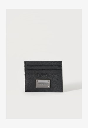 Porte-cartes en cuir noir avec quatre emplacements pour cartes et une plaque métallique gravée du nom de la marque sur fond blanc.
