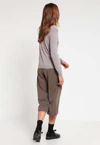 Hellgraues langärmliges Oberteil mit eng anliegenden Bündchen, kombiniert mit lockeren, olivgrünen, gekürzten Hosen, getragen mit schwarzen Socken und Schuhen.