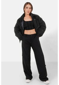 Zwarte pufferjas met hoge kraag en rits, gedragen over een zwarte crop top. Zwarte wijde broek, met zakken en een ontspannen pasvorm.