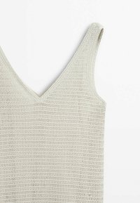 Débardeur blanc sans manches en maille avec col en V, présentant un motif texturé en maille ouverte, affiché sur un fond blanc uni.